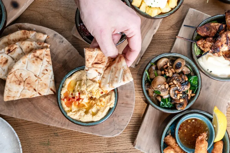 Various small dishes on a table. Someone dipping pita bread into one.