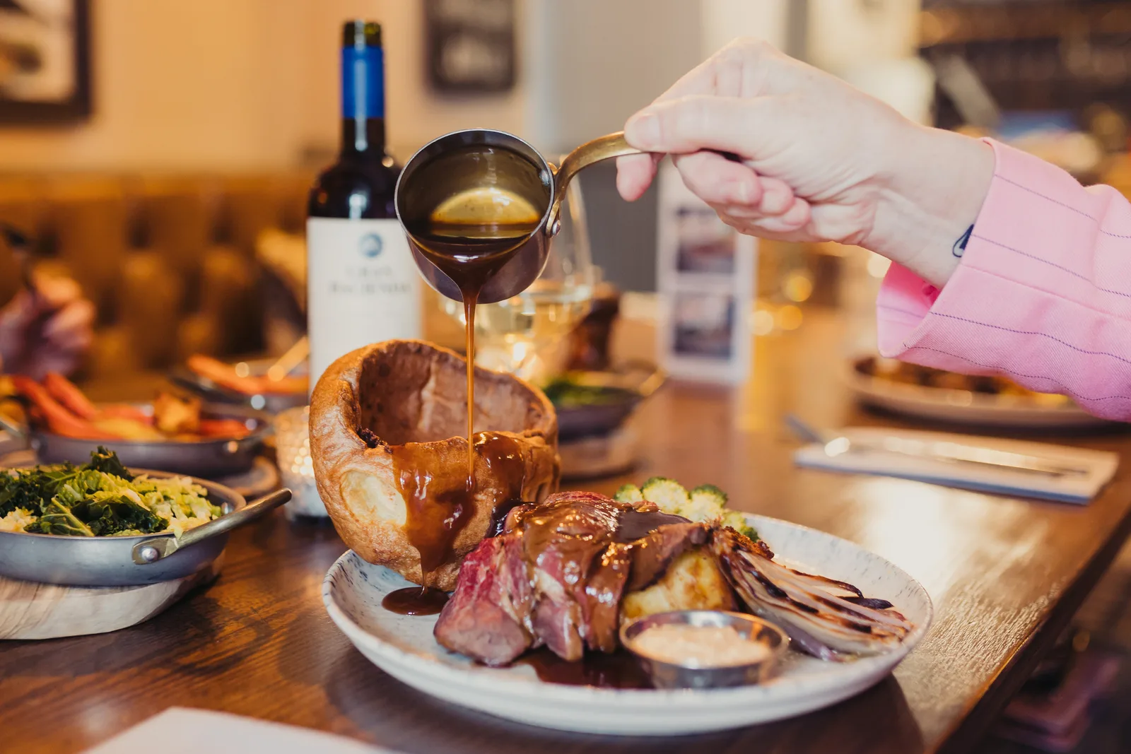 Pouring gravy on a plate with yorkshire puddings and beef