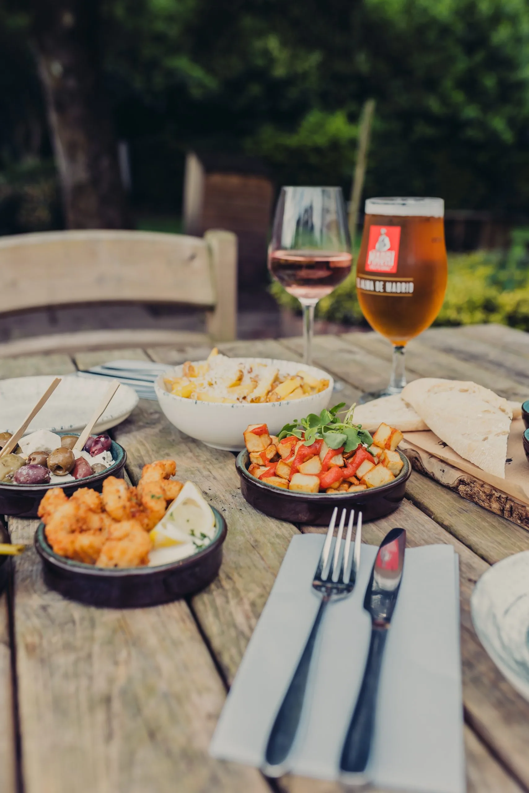 Table situated outside with several dishes and two wine glasses. There is also a knife and fork on a napkin