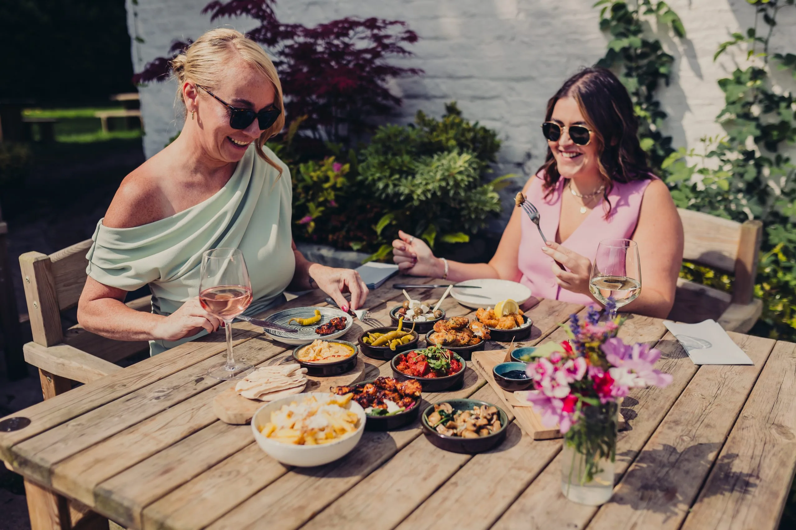 Two ladies sitting at the table. The table has various dishes on it.