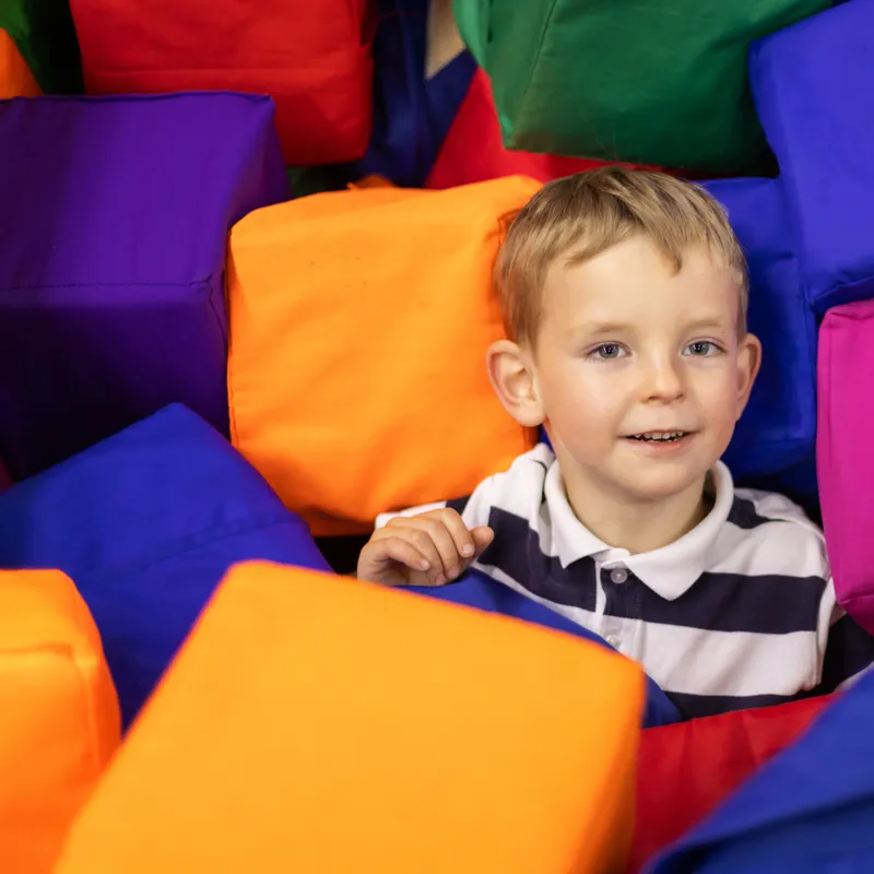 A young boy smiling at the camera in between various colourful blocks