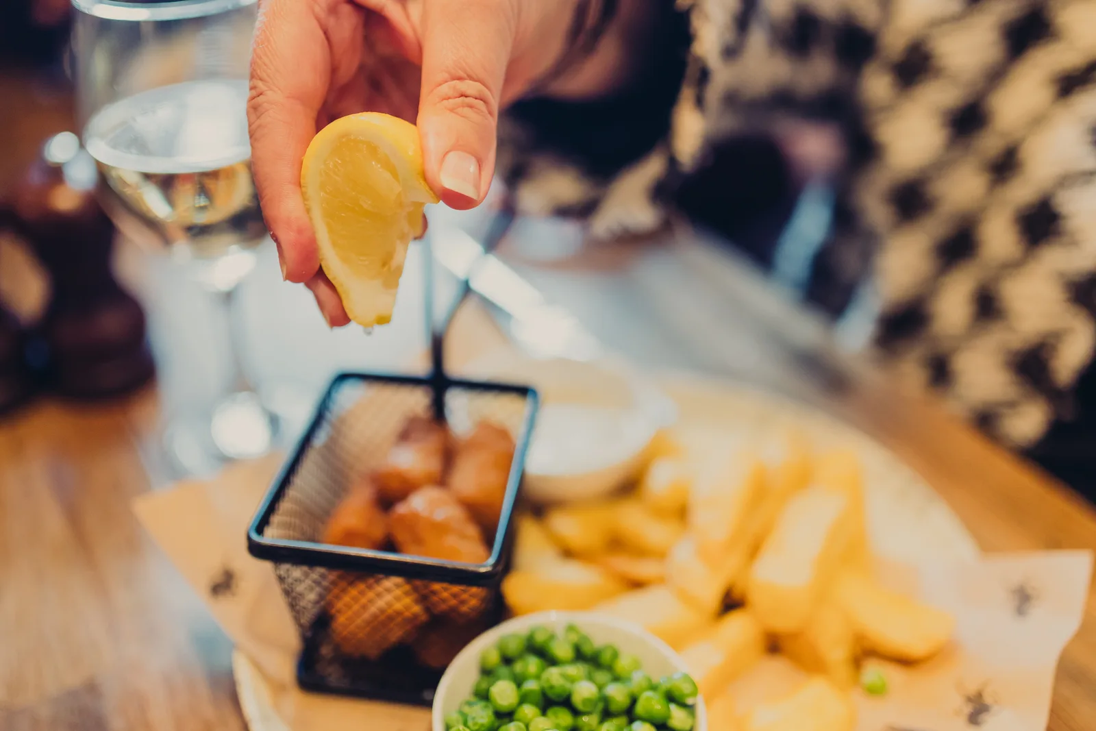 A person squeezing a lemon with chips and peas in the background
