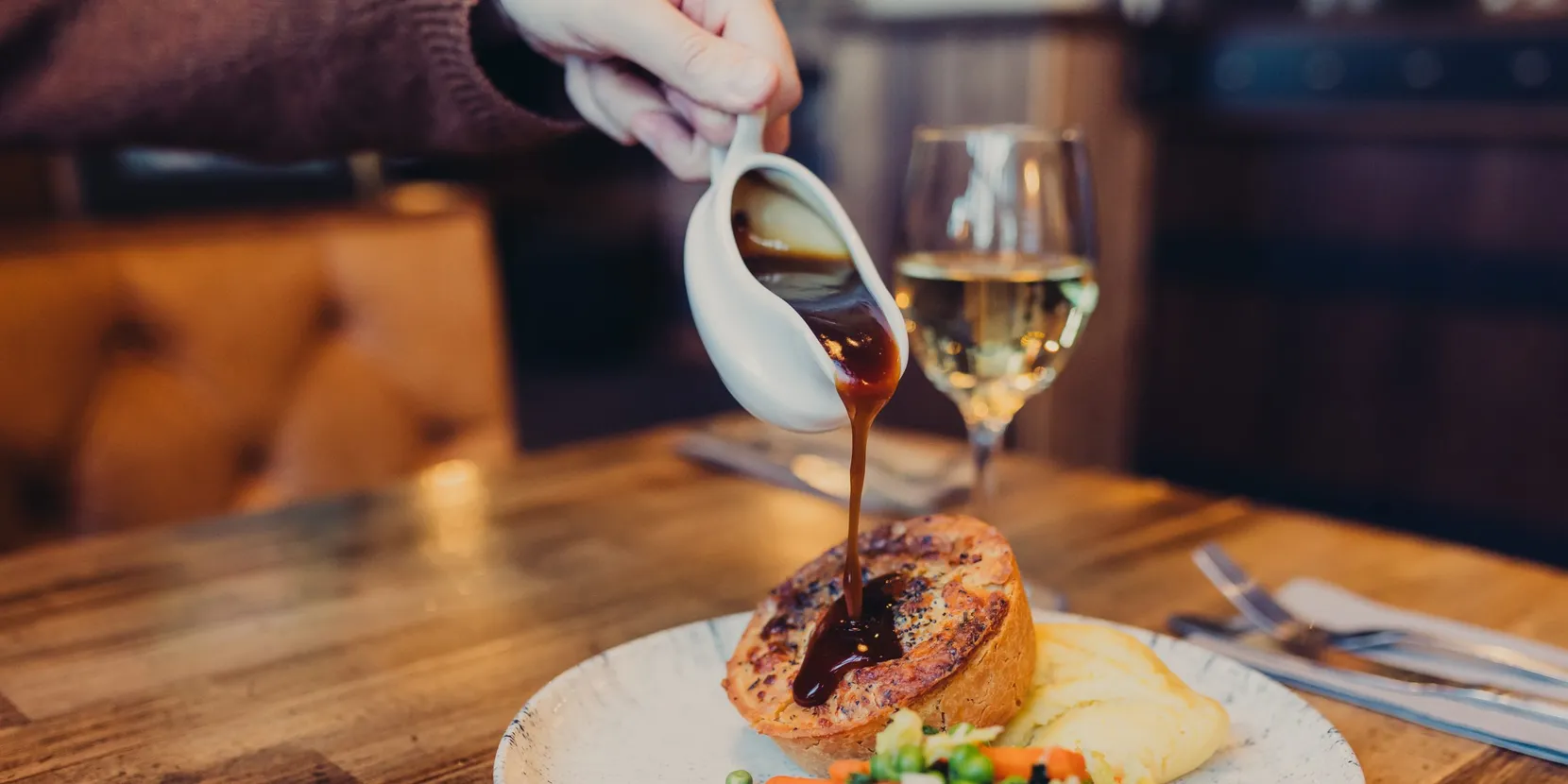 Someone pouring gravy onto a plate with pie